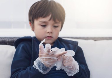 Seçici odaklı küçük çocuk kanepede plastik eldiven takıyor, okul öncesi çocuğu evde oynarken eğleniyor, eğitim konsepti var.