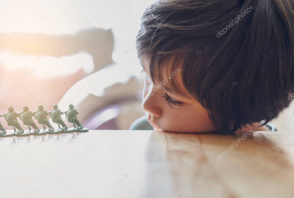 High key light portrait of lonly kid boy with sad face playing alone, Bored Child lying head donw on table looking at soldier toy with morning bright light background
