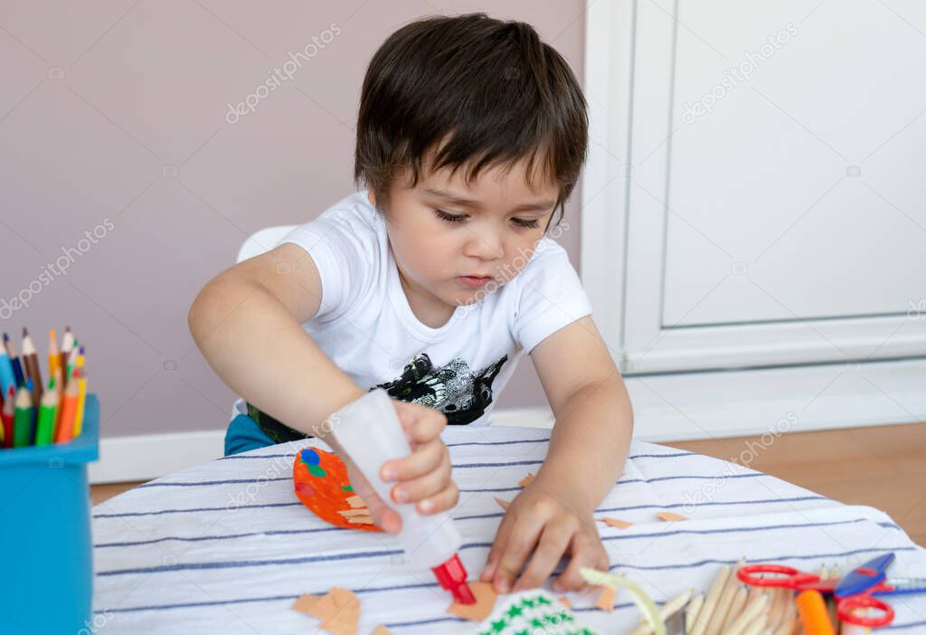  little boy making Easter greeting card,Materials for art creativity on kid table, 3 years old boy gluing on color paper, Crafts activity in kindergarten with parents, Home schooling concept