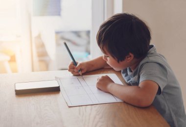 Ödevi için cep telefonu kullanan anaokulu çocuğunun portresi, ev ödevi yaparken cep telefonu araması yapan çocuğun seçmeli odağı, internet ve evde eğitim kavramı.