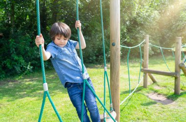 Aktif çocuk oyun parkında ip tırmanıyor, yaz güneşli bir günde macera parkında eğlenen çocuk, dışarıda oyun alanında eğlenen sevimli küçük çocuk..