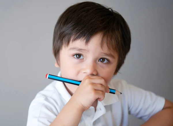 Cropped shot of school kid holding pencil and looking up with deep in throught, Child boy sitting alone with curious face doing homework. Education concept