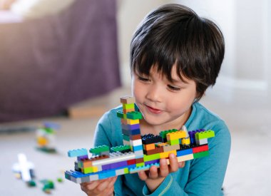 Plastik oyuncak bloklarıyla oynayan aktif çocuk, evde renkli oyuncaklarla oynayan çocuğun seçici odağı, bebek gelişimi konsepti.