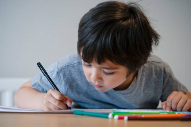 Evde ödev yapan anaokulu çocuğunun portresi. Mutlu Çocuk renkli kalemlerle çiziyor, Küçük çocuk masada yazıyor, ilkokul ve eğitim konsepti.