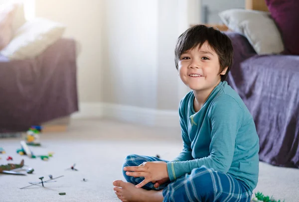 Happy kid boy sitting on carpet floor playing with soldiers and figurine toys inliving room, Selective focus Child playing wars and peace on his own at home, Children imagination and development