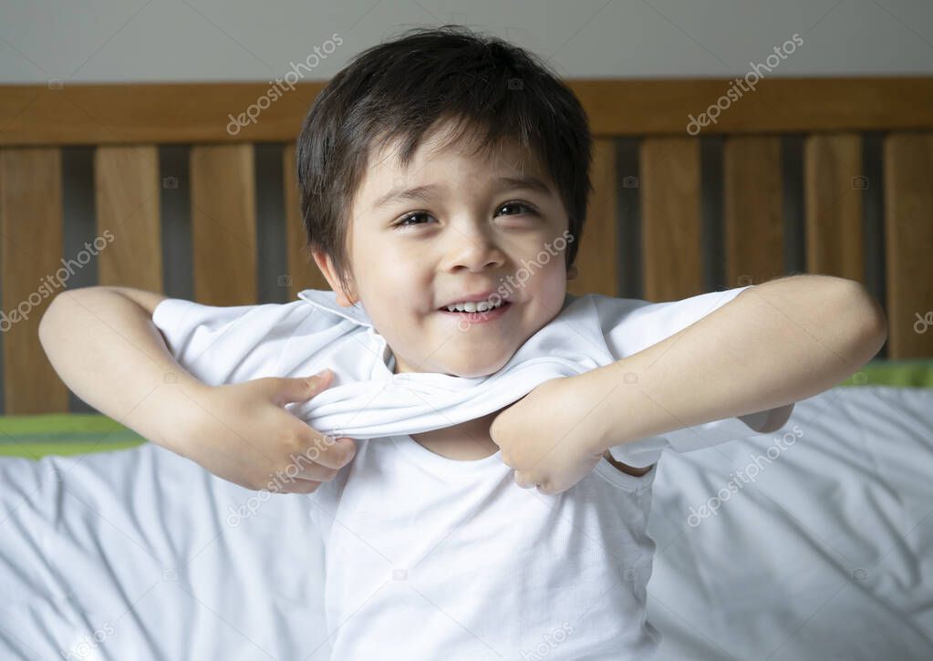 School boy sitting in bed and try to wearing his cloth with smiling face,Cute kid boy getting dressed and get ready for school,Child dressing uniform in bed room ready to school,Back to school concept