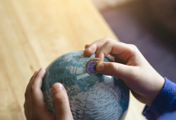 Kid hand putting one pound coin into piggy bank to donate money helping the earth, Hand holding money, Children learning to save money for sharing, studying, traveling or future with new normal life