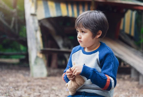 Yalnız çocuğun portresi, elinde köpek oyuncağı, parkta tek başına oturuyor, üzgün çocuk oyuncağıyla oturuyor ve düşünen yüzüyle bakıyor, mutsuz yüzüyle tek başına oynayan küçük çocuk..