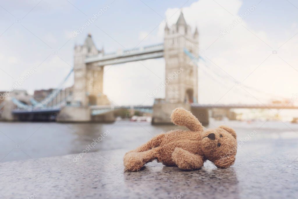 Teddy bear lying alone with blurry london tower bridge background, The forgotten bear sitting by the river, lost property, Lonely concept, Lost child, International missing child