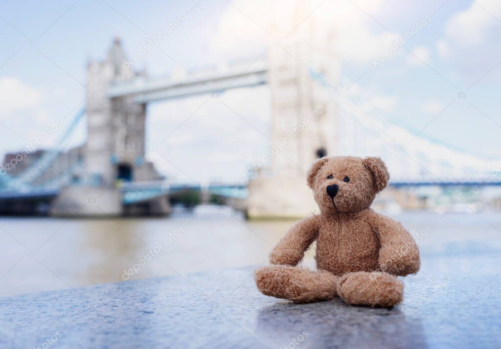 Teddy bear sitting alone with blurry london tower bridge background, The forgotten bear sitting by the river, lost property, Lonely concept, Lost child, International missing child