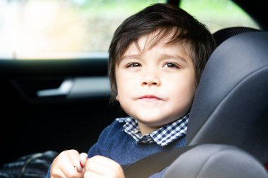 Portre kesilmiş küçük bir çocuk emniyet koltuğunda oturan sevimli bir çocuk bebek koltukta oturan kemeri takılı çocuk elinde şeker tutarak arabadan dışarı bakıyor çocuk taşımacılığı güvenliği.