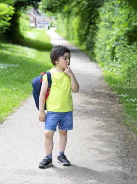 Kid with standing alone and puting finger on his mouth with bored face, Unhappy kid get bored waiting for school bus, School boy carrying backpack get ready for school summer camp clipart