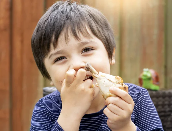 Lezzetli yüzlü şirin bir çocuğun portresi bahçede kızarmış tavuk budu yemekten, ızgara tavuk yemekten, çocuk için sağlıklı yiyecekler kavramından zevk alır.