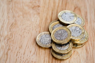 Yeni İngiliz 1 pound sikkelerine yakın çekim, İngiliz sterlin paralarının seçici odak noktası ahşap masa..