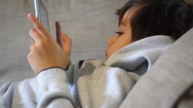 Candid tablette çizgi film izleyen sevimli bir çocuğu, kanepede uzanmış akıllı telefonda ciddi yüz oyunları oynayan bir çocuğun portresini çekti. Evdeki sıcak ve samimi sahne