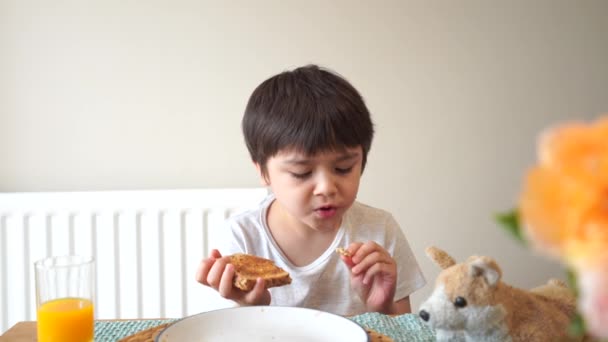 在上学前 健康的孩子在烤橙汁中吃蜂蜜 在早餐时吃橙汁 形象的孩子在吃多面面包时很开心 健康的孩子在吃概念 — 图库视频影像