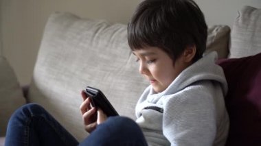 Ödevi için cep telefonu kullanan bir çocuk, internetten arkadaşıyla cep telefonu konuşması yapan bir çocuk, kapalı alan, evde eğitim, sosyal mesafe, e-öğrenim online eğitim.