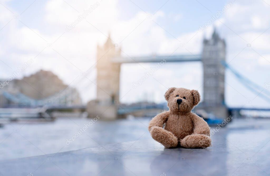 Teddy bear sitting alone with blurry london tower bridge background, The forgotten bear sitting by the river, lost property, Lonely concept, Lost child, International missing child