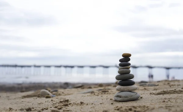 Pebble tower by the seaside with blurry pier down to the sea in Stack of zen rock stones on the sand, Stones pyramid on the beach symbolizing, stability, harmony, balance with shallow depth of field.