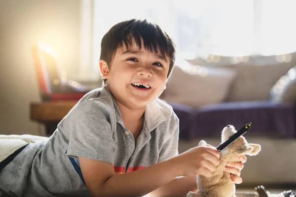 柔らかいおもちゃで遊ぶ床の上に横たわる肖像画の子供 週末にリビングルームでリラックスしたカーペットの上に横たわる幸せな子供の男の子 カメラを見て笑顔の顔を持つ若い男の子 肯定的な子供の概念 — ストック写真