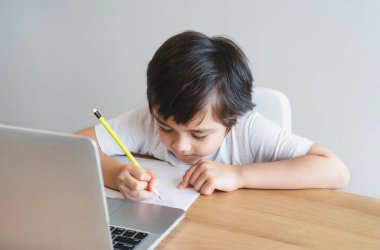 Ev ödevi olarak bilgisayar kullanan yeni normal okul çocuğu, evde çalışması, sosyal uzaklık, E-öğrenim çevrimiçi eğitim kavramı için dizüstü bilgisayarı kullanarak İnternet 'te araştırma yapan çocuk.