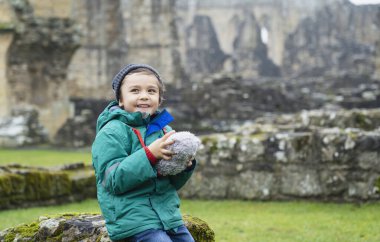 Okullu çocuğun oyuncak ayıyı öğrenme geçmişiyle keşfe çıkardığı portresi yumuşak oyuncağını eski manastır arka planının bulanık kalıntılarıyla eski tuğla duvarda tutan sıcak giysiler giyen mutlu çocuk.