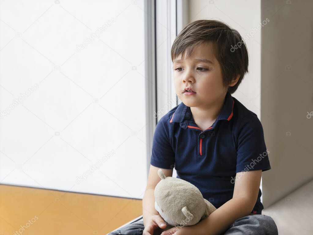 Emotional portrait sad kid sitting with teddy bear, Lonely kid sitting on floor in corner and looking down,Little boy wall corner punishment sitting,Family violence concept.