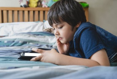 Çocuk ödevi için tablet kullanıyor, çocuk yatakta dijital dokunmatik kâğıtta oyun oynuyor, küçük çocuk tabletle yatıyor. Evde eğitim, sosyal mesafe, e-öğrenim çevrimiçi eğitim.