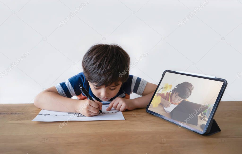 School Kid using pen drawing cartoon on paper, Child sitting alone doing home work, Young boy using digital pad searching information on internet for his study at home, E-learning online education 