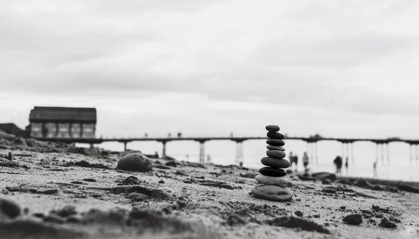 Pebble tower by the seaside with blurry pier down to the sea, Stack of zen rock stones on the sand, Stones pyramid on the beach symbolizing, stability, harmony, balance with shallow depth of field.