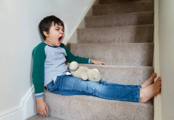 Portre yorgun çocuk merdivenlerde esniyor, uykulu çocuk oyuncak ayıyla oynarken esniyor, çocuğun hava değişimi sırasında alerjisi var, çocukluk dönemi toz maytunun yansıması ya da saman nezlesi olabilir.