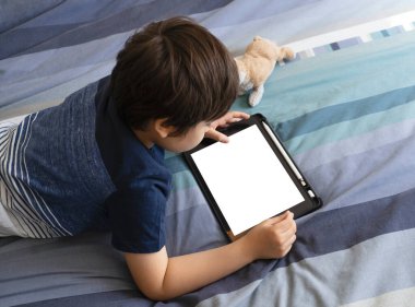 Yatakta yatan çocuk, yatak odasındaki dijital dokunmatik kâğıtta oyun oynuyor, küçük çocuk tabletle yatıyor. Evde eğitim, sosyal mesafe, e-öğrenim çevrimiçi eğitim
