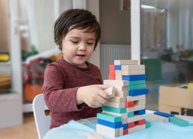 Neşeli küçük çocuğun gizli çekimleri oyun odasında renkli tahta bloklar, evdeki tahta blokları istifleyen çocuk portresi, anaokulu ve anaokulu çocuğu için eğitici oyuncaklar. Yaratıcı kavram