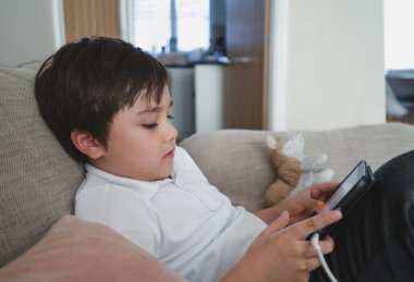 Çocuk kanepede oturup cep telefonuyla çizgi film izliyor, okul çocuğu cep telefonlarını kullanarak internet, evde eğitim, uzaktan eğitim kavramını kullanıyor.