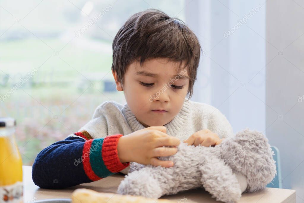 High key light portrait cute boy plying teddy bear on table, Adorable Child playing with toys and relaxing while waiting for food in cafe.