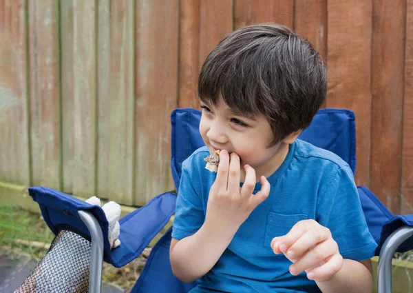 庭でハンバーガーの肉ボールを食べる子供 空腹の子供の男の子彼の自家製のピクニックフード 春または夏の屋外活動を食べる外に座って — ストック写真