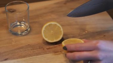 Bir limonu ahşap kesme tahtasıyla doğramak ve büyük bir mutfak bıçağıyla yakın plan bir bardağa sıkıştırmak.