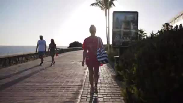 Um hiperlapso de uma mulher em um vestido rosa andando por um passeio de férias ao sol — Vídeo de Stock