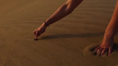 Gün batımında kuma kalp çizen genç bir kadının yavaş çekim videosu.
