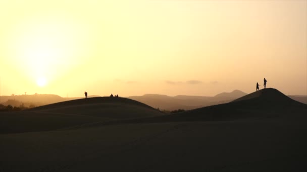 멀리 서 해 가질 때 모래 언덕을 거닐고 있는 실루엣 — 비디오