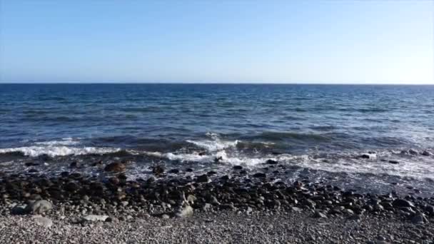 En stillbild av vågorna som långsamt kraschar på stenstranden på en strand på sommaren med klarblå himmel — Stockvideo