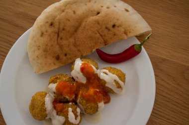 Falafel, geleneksel İsrail yemekleri. Tahini ve harissa soslu falafel tabağı, kırmızı biber ve pide ekmeği. Üst görüntüdeki taze malzemeler. Sağlıklı yeme kavramı. 