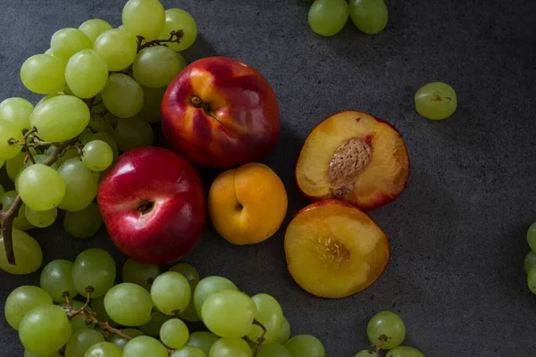 美丽的夏天水果放在桌子上 多汁的油桃 绿色葡萄和梨的顶部照片 带有复制空间的深灰色背景 — 图库照片