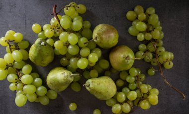 Yeşil üzümler ve armutlarla dolu bir hayat. Koyu gri desenli arka plan. Taze yaz meyveleri üst görünüm fotoğrafı.