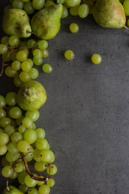 Koyu gri desenli arka planda yeşil üzüm ve armutlar. Yaz meyveleri sınırı. Fotokopi alanı olan güzel üst görüntü fotoğrafı. 