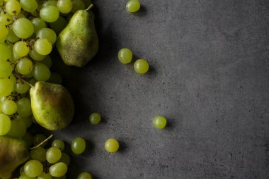 Koyu gri desenli arka planda yeşil üzüm ve armutlar. Yaz meyveleri sınırı. Fotokopi alanı olan güzel üst görüntü fotoğrafı. 