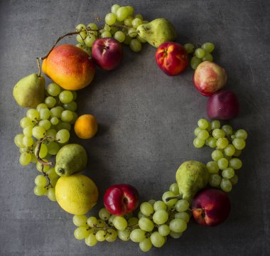 Yaz meyvesi kompozisyonu. Renkli üzümler, nektarinler, mango ve armut çelenk üst manzara fotoğrafı. Kopya alanı ile koyu gri desenli arkaplan. 