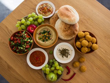 Ortadoğu 'nun otantik yemekleri. Bir tabak humus, falafel, pide, harissa sosu, tahini, taze salata ve ahşap masada meyveler. Geleneksel İsrail yemekleri. Fotokopi alanı olan güzel yemek resmi.