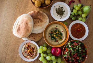 Ortadoğu 'nun otantik yemekleri. Bir tabak humus, falafel, pide, harissa sosu, tahini, taze salata ve ahşap masada meyveler. Geleneksel İsrail yemekleri. Fotokopi alanı olan güzel yemek resmi.