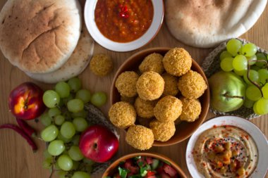 Ortadoğu 'nun otantik yemekleri. Bir tabak humus, falafel, pide, harissa sosu, tahini, taze salata ve ahşap masada meyveler. Geleneksel İsrail yemekleri. Fotokopi alanı olan güzel yemek resmi.